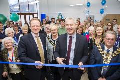 Man cuts the ribbon with a large group of people behind 